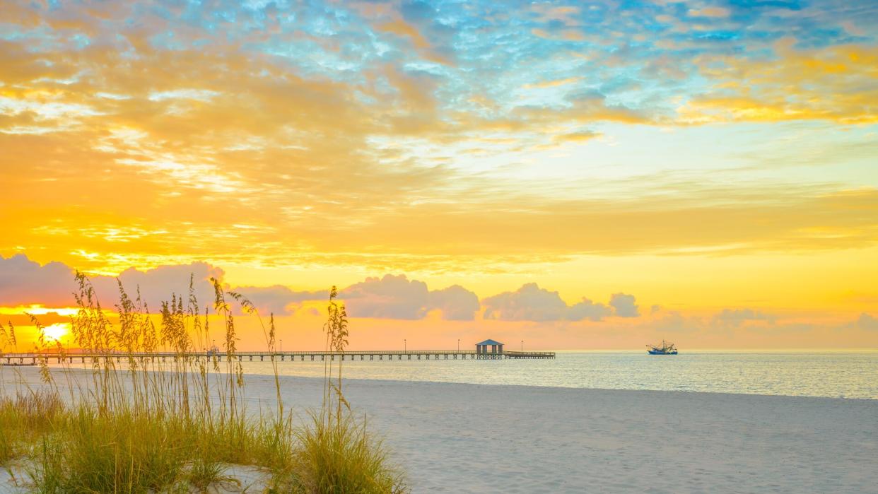 Gulfport Mississippi beach, dramtic golden sunrise, pier, shrimp boat, on the Gulf of Mexico.