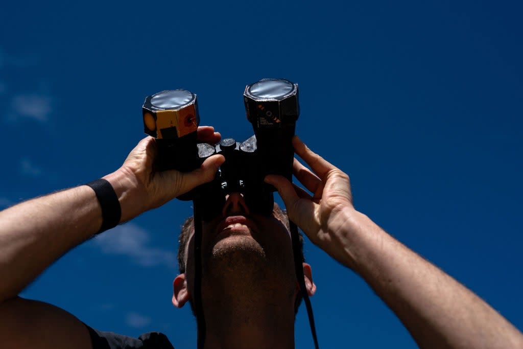 Frederik De Vries who is visiting from Amsterdam, looks up at the sun using binoculars outfitted with solar film, as people gather on the National Mall to view the partial solar eclipse on 8 April, 2024 in Washington, DC (Getty Images)