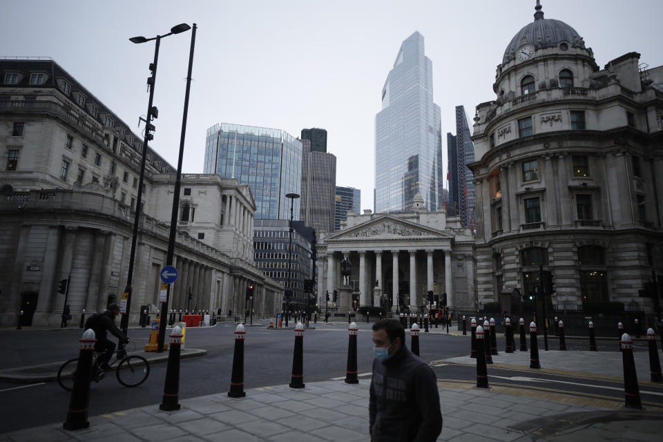 A man wearing a face mask to curb the spread of coronavirus walks backdropped by the Bank of England, left, and the Royal Exchange, centre, in the City of London financial district in London, Jan. 5, 2021, on the first morning of England entering a third national lockdown since the coronavirus outbreak began. British Prime Minister Boris Johnson on Monday night announced a tough new stay-at-home order that will last at least six weeks, as authorities struggle to stem a surge in COVID-19 infections that threatens to overwhelm hospitals around the U.K. (AP Photo/Matt Dunham)