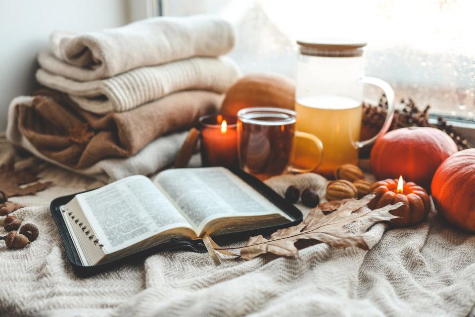 open bible in autumn interior with blankets, tea, candles and pumpkins in front of window