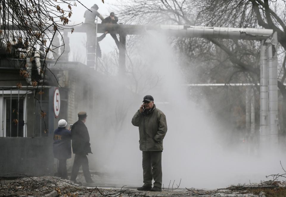 A man talks on a phone as workers repair a heating pipeline at a site hit by shelling in Donetsk, eastern Ukraine, February 1, 2015. REUTERS/Maxim Shemetov (UKRAINE - Tags: POLITICS CIVIL UNREST CONFLICT)