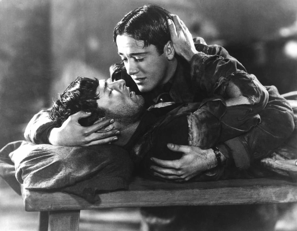 Scene from an old movie with two characters in an emotional embrace, one lying down with head supported by the other