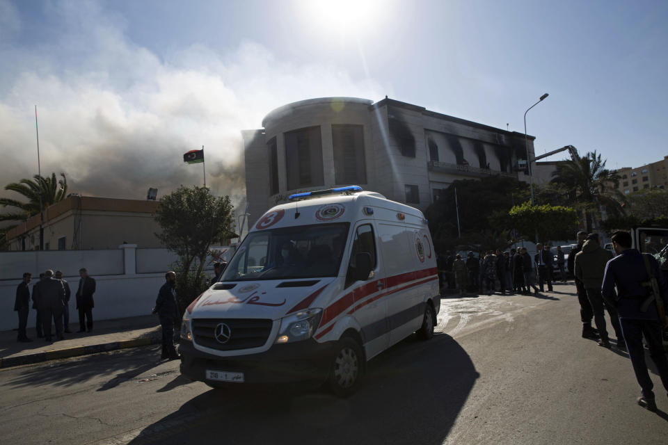 An ambulance carries injured as smoke rises following a deadly attack on the foreign ministry building, in Tripoli, Libya, Tuesday, Dec, 25, 2018. Security officials said Tuesday that a suicide bomber targeted the entrance of Libya’s Foreign Ministry in Tripoli, killing several people, including a prominent militia leader. They said a second attacker was shot dead by guards before he could detonate his explosive vest. (AP Photo/Mohamed Ben Khalifa)