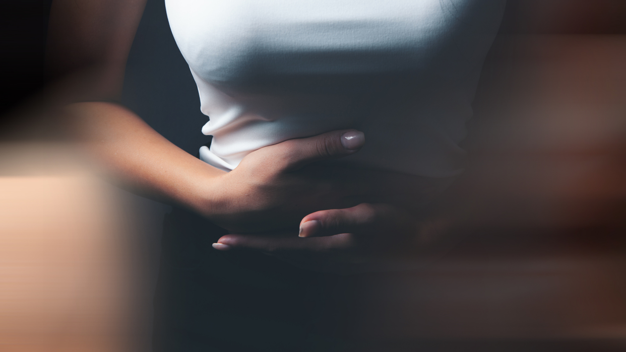 What is a decidual cast? A woman in a sleeveless white top clutches her midriff in apparent pain.