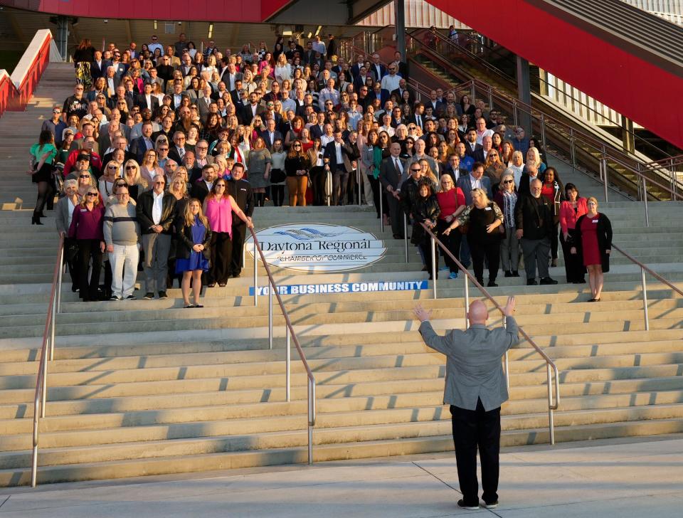 Ken Phelps, vice president of resource development for the Daytona Regional Chamber of Commerce, directs members as they gather for a group photo on the steps of Daytona International Speedway prior to the start of the chamber's 104th annual meeting on Friday, Feb. 2, 2024. The event, which drew more than 600 people, featured a talk and performance by country music superstar Brian Kelley who grew up in Ormond Beach.