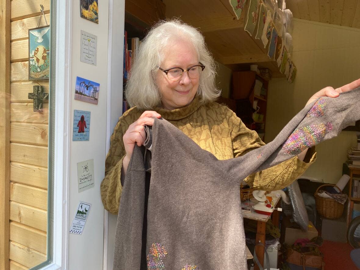 Textile artist Heather Cameron stands in front of her Gabriola Island studio, holding a sweater she mended.  (Margaret Gallagher/CBC - image credit)