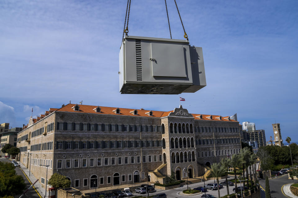 With the Lebanese Government House in the background, a new generator is hauled up to the roof of an office building, in Beirut, Lebanon, Feb. 21, 2022. They literally run the country. Private generators are ubiquitous in parts of the Middle East, spewing hazardous fumes into homes and business across the country, almost 24 hours a day. As the world looks for renewable energy to tackle climate change, Lebanon, Iraq, Gaza and elsewhere rely on diesel-powered private generators just to keep the lights on. (AP Photo/Hassan Ammar)