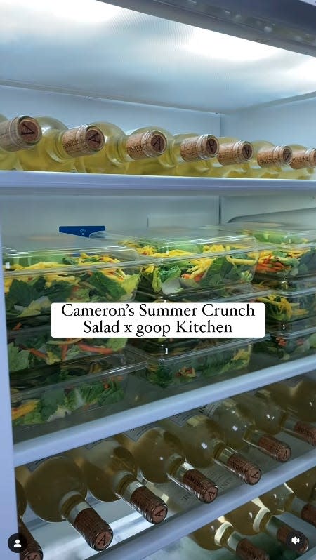a pristine fridge with numerous bottles of avaline white wine on the top and bottom shelves, and stacked boxes of salad on the middle shelf. text over the video reads "cameron's summer crunch salad x goop kitchen"