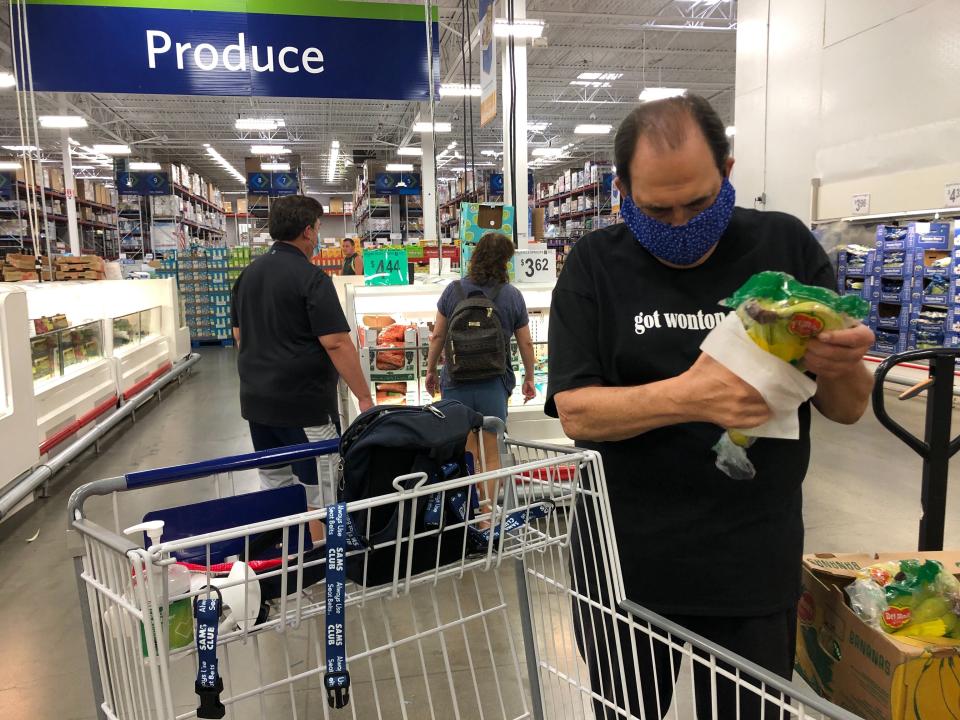 In this Tuesday, March 31, 2020 photo, comedian Frank De Lima wears a masks and maintains social distancing while wiping a package of bananas at a Sam's Club store in Honolulu. People in Hawaii are changing how they express aloha in the time of coronavirus. Some residents say social distancing is the antithesis of tradition in the state, where people greet each other with hugs, kisses and lei, and families are close-knit. (AP Photo/Jennifer Sinco Kelleher)