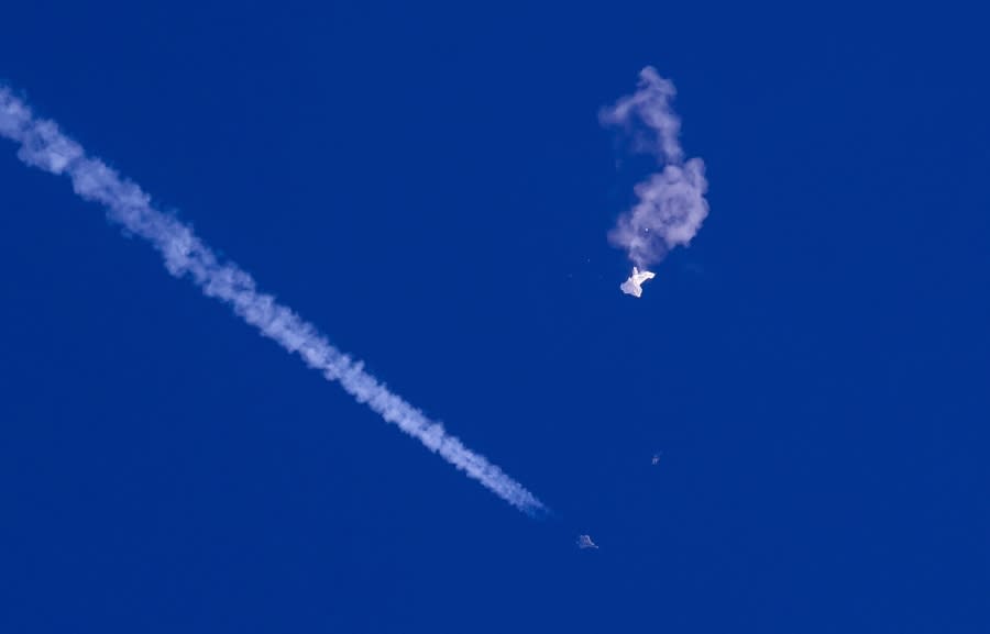 In this photo provided by Chad Fish, the remnants of a large balloon drift above the Atlantic Ocean, just off the coast of South Carolina, with a fighter jet and its contrail seen below it, Saturday, Feb. 4, 2023. The downing of the suspected Chinese spy balloon by a missile from an F-22 fighter jet created a spectacle over one of the state’s tourism hubs and drew crowds reacting with a mixture of bewildered gazing, distress and cheering. (Chad Fish via AP)