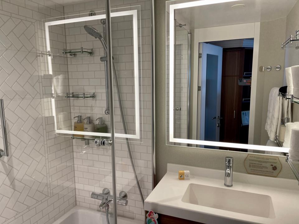 A bathroom in one of the Disney cruise rooms with a light-up mirror, sink, and shower.