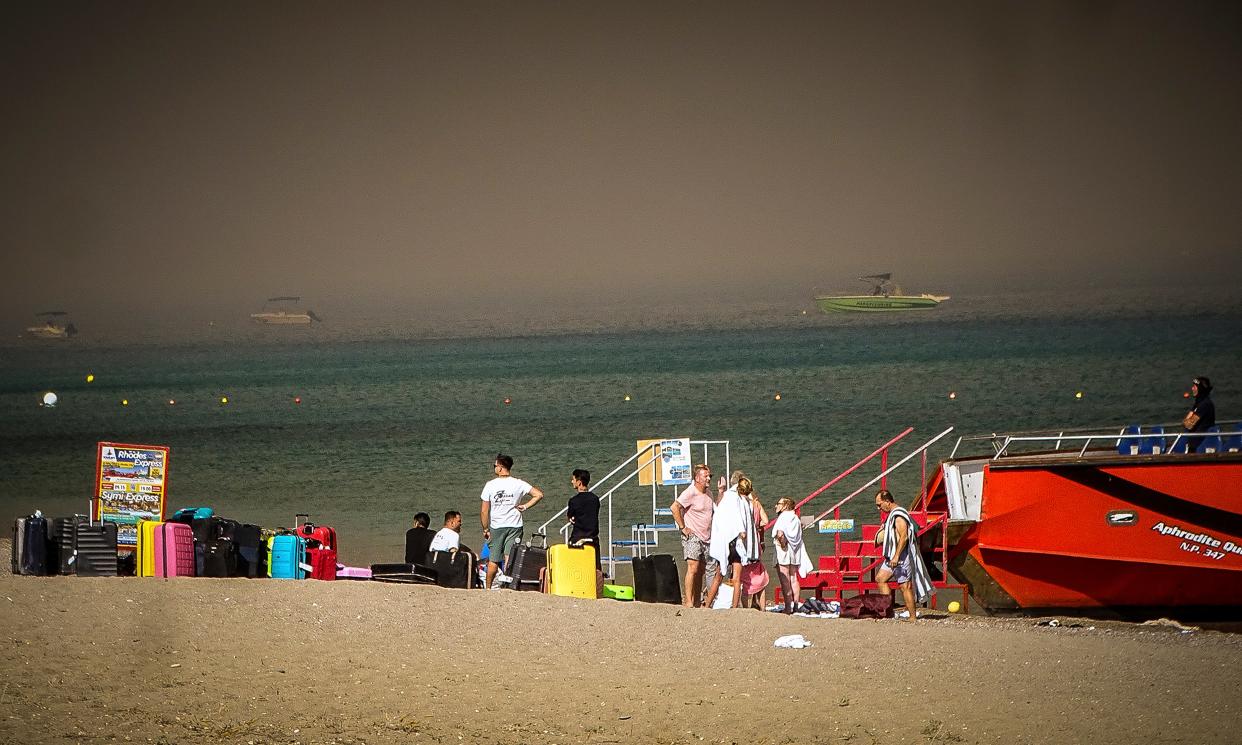 Tourists stand on a beach after being evacuated (AP)