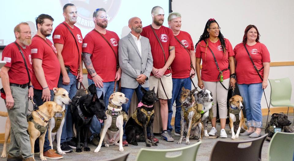 Healing Paws for Warriors co-founder Mike Arena, in gray, stands with graduate teams for a group photo during their graduation ceremony. Evan Williams Bourbon recently honored Arena as a 2022 American-Made Hero, making him part of a select group of veterans to be featured on the limited-edition Evan Williams American Hero bottles.