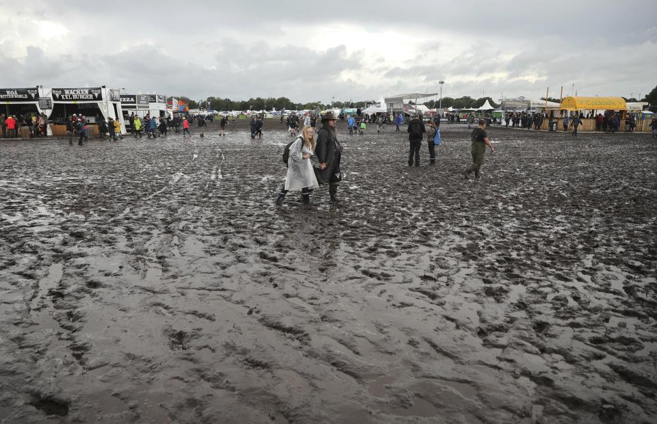 Metal fans walk on the muddy festival grounds ahead of the beginning of the Wacken Open-Air (WOA) Festival, in Wacken, Germany, Tuesday Aug. 1, 2023. WOA Festival takes place from August 2 to August 5, and is considered the largest heavy metal festival in the world. (Christian Charisius/dpa via AP)