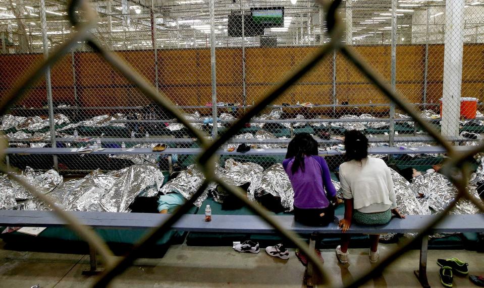 Niñas ven la televisión mientras otras duermen en el suelo cubiertas de mantas de material metálico término dentro de un centro de detención de menores indocumentados en EEUU. (AP)