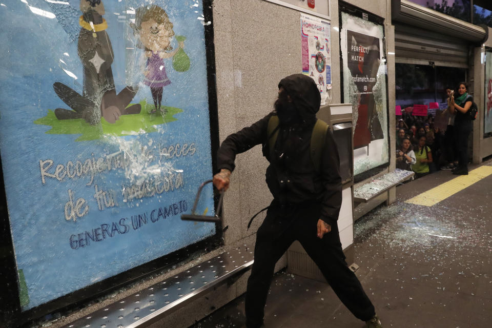 A masked protester damages a glass of a bus station advertisement using a bike lock during a protest sparked by a string of alleged sexual attacks by police officers, in Mexico City, Friday, Aug. 16, 2019. On Friday, hundreds of women demonstrated largely peacefully in downtown Mexico City with pink spray paint and smoke. But some protesters trashed a bus station. This week, an auxiliary policeman was held for trial on charges he raped a young female employee at a city museum. (AP Photo/Marco Ugarte)