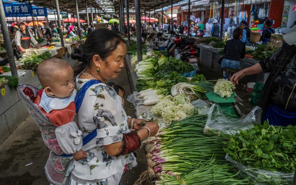 A woman from the Bai ethnic group carries a baby on her back as she buys goods at a local market on April 24, 2021 in Xizhou, Yunnan province, China - Kevin Frayer /Getty Images AsiaPac 