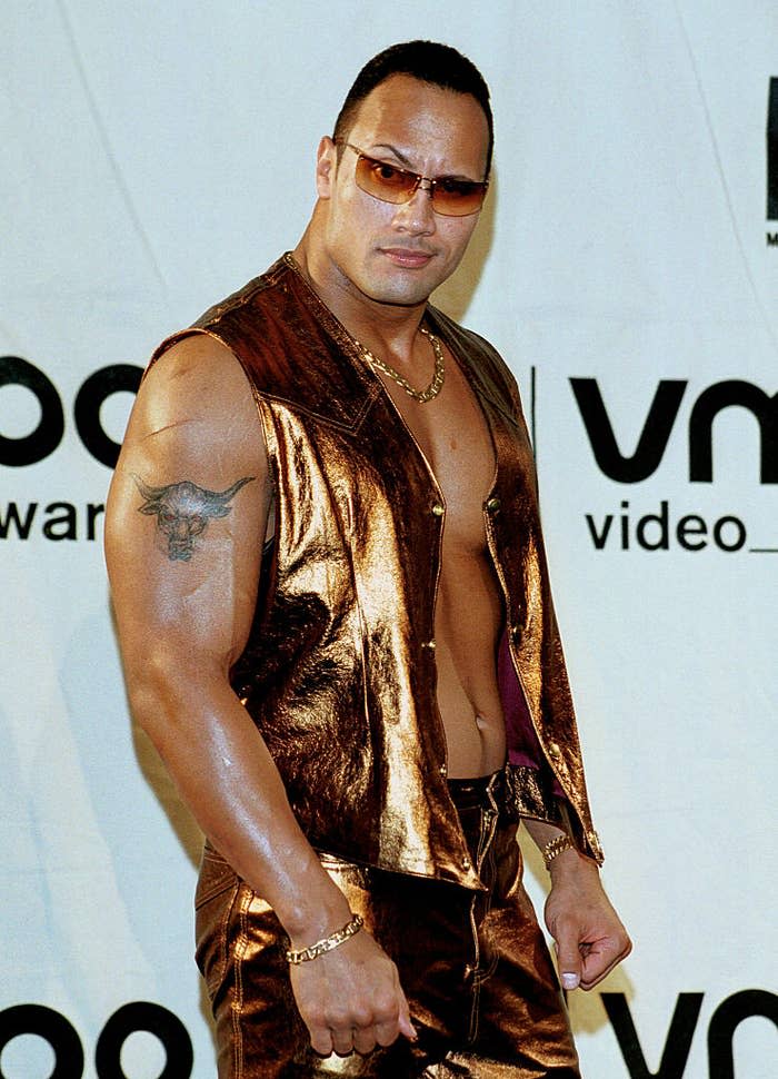 Dwayne "The Rock" Johnson poses at the MTV Video Music Awards in a metallic outfit with sunglasses and a sleeveless vest, showcasing his arm tattoo