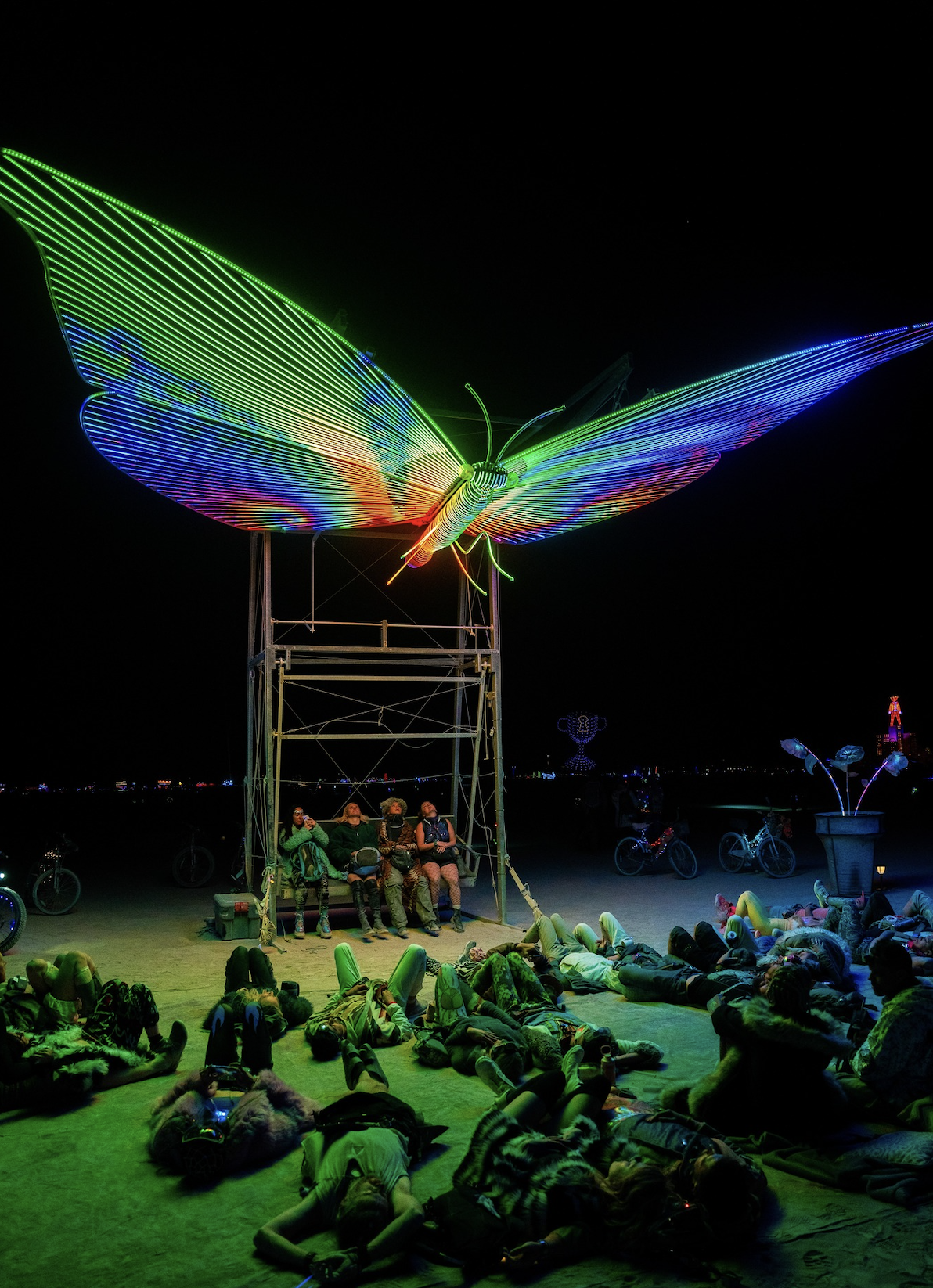 Burners relax under a mesmerizing neon butterfly beneath the desert sky.