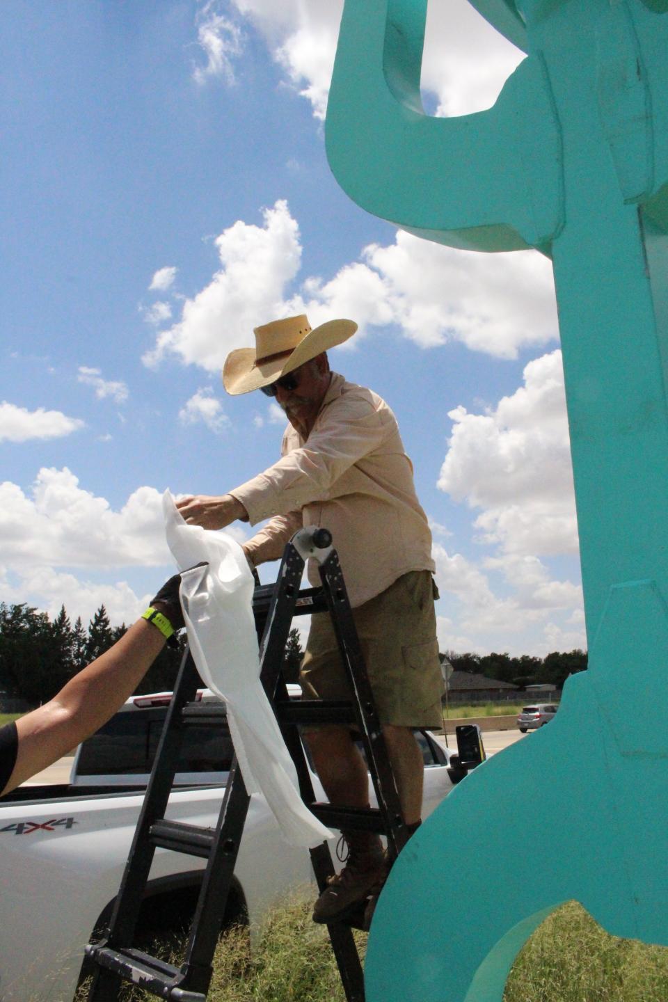 Artist B.C. Gilbert works to unveil the Blue Cowboy, which is now on display at Spur 327 and Loop 289.