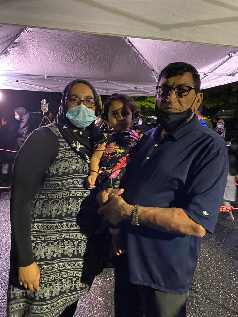 In this photo taken by Nita Mukhi, Fatima Mukhi-Siwji, her daughter Aliyah and father Firoz Mukhi pose at a drive-in commemoration of the 7th century death of Imam Hussein, Aug. 27 2020 in Hicksville, New York. Shiite Muslims are marking the mourning period in the shadow of the coronavirus. (Nita Mukhi via AP)