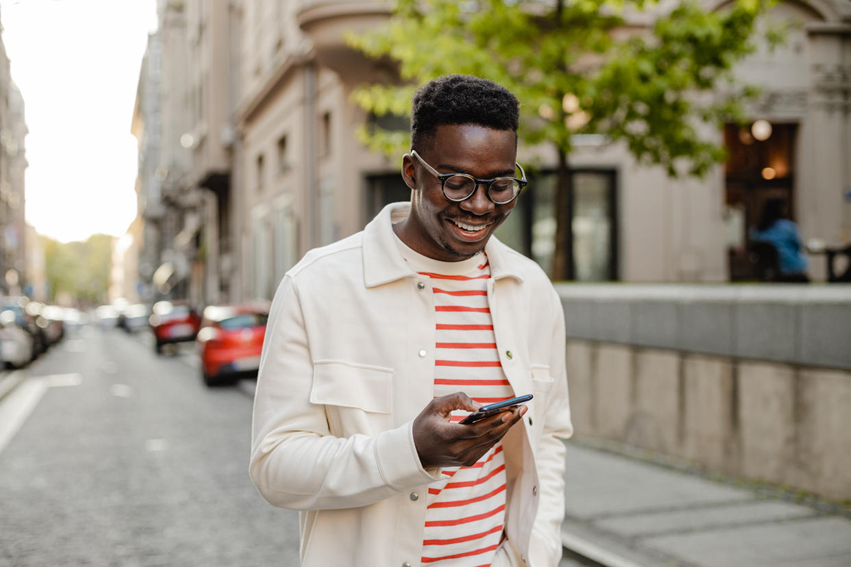 The portrait of an African-American man is on the street, he is walking and using a mobile phone on the go