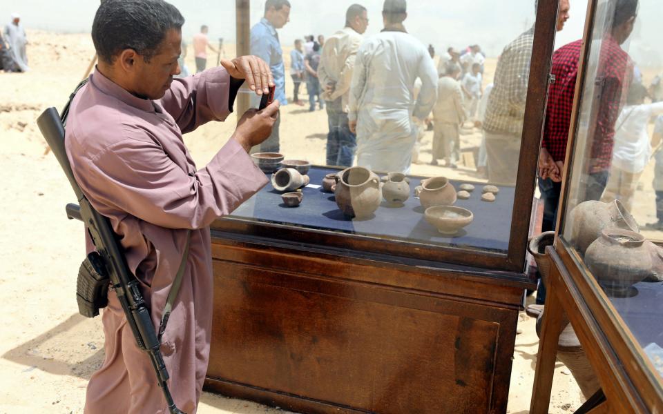 A policeman takes a photograph of objects that were found inside a burial site in Minya, Egypt - Credit: AFP