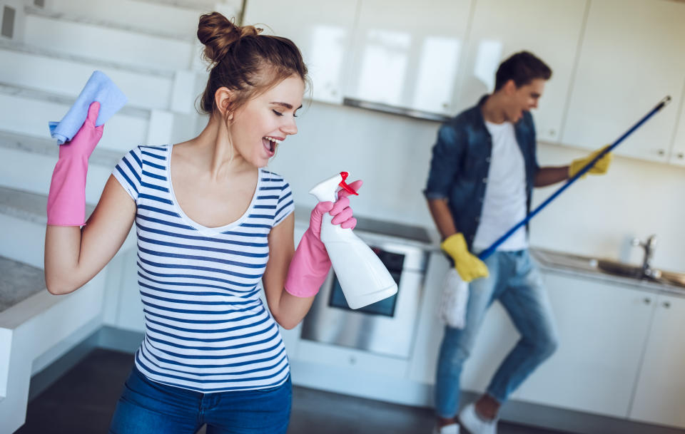 A man and a woman dancing while cleaning their house with gloves on.