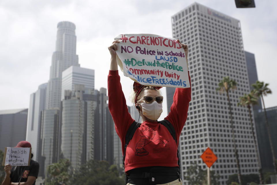 FILE - A demonstrator holds a sign in front of the downtown skyline during a protest to demand the defunding of the Los Angeles school district police outside of the school board headquarters Tuesday, June 23, 2020, in Los Angeles. The Los Angeles City Council has voted to slash the Police Department budget by $150 million, reducing the number of officers to a level not seen for more than a decade. The council approved the change Wednesday, July 1, 2020, dropping the number of officers to a little more than 9,700 by next summer. (AP Photo/Marcio Jose Sanchez, File)