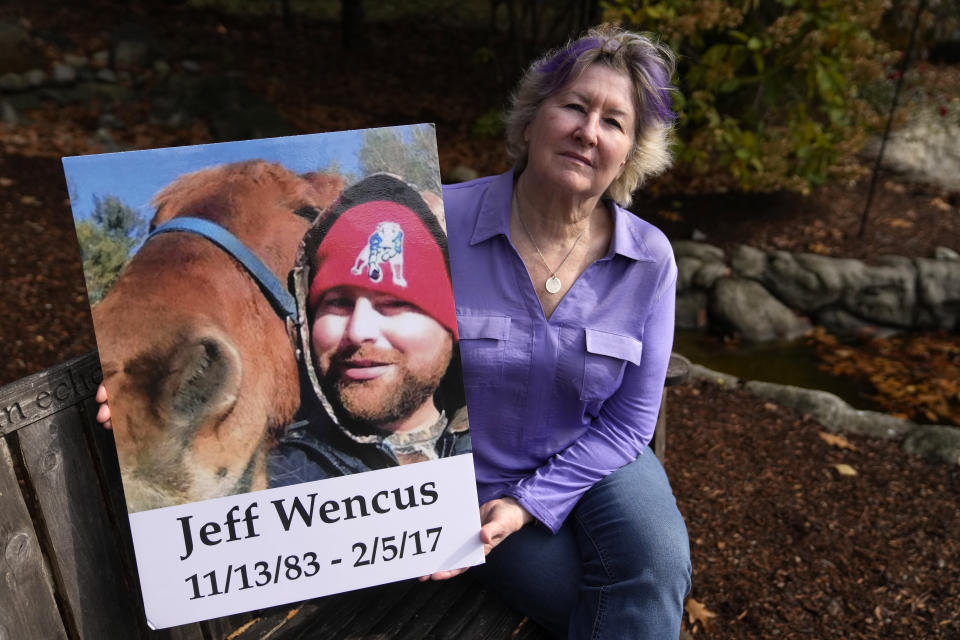 Lynn Wencus, of Wrentham, Mass., holds a photograph of her son Jeff while seated in a garden at her home, in Wrentham, Tuesday, Nov. 7, 2023. Wencus lost Jeff to a heroin overdose in 2017. Families who lost loved ones to overdose are divided over OxyContin maker Purdue Pharma's plan to settle lawsuits over the toll of opioids with governments. It could provide billions to address an overdose epidemic and pay some victims. But it would also protect members of the Sackler family who own the company from future lawsuits. (AP Photo/Steven Senne)