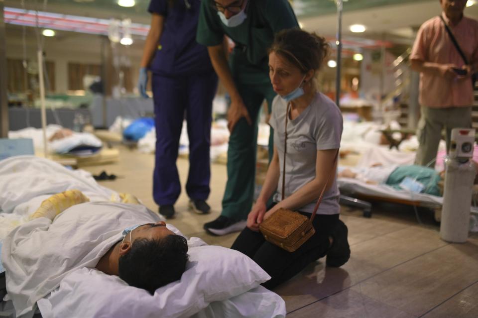 A woman sits next to a patient on the floor of a ferry boat after health authorities partially evacuated a hospital in Alexandroupolis, in the northeastern Evros region, Greece, early Tuesday, Aug. 22, 2023. Gale-force winds fanned the flames of wildfires across Greece, including more than four dozen new blazes that broke out Monday amid hot, dry and windy weather that has sucked moisture from vegetation. (e-evros.gr via AP)