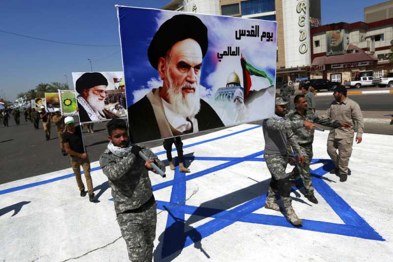 伊朗與以色列衝突加劇，可能影響其他中東地區。2017年6月23日，伊拉克民兵舉著伊朗已故領袖何梅尼的肖像，踩過以色列國旗。（AP）