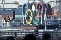 A police officer patrols near the Olympic Symbol being transported on a barge in the Odaiba section Tuesday, Dec. 1, 2020, in Tokyo. The five Olympic rings are back in Tokyo Bay. They were removed for maintenance four months ago shortly after the Tokyo Olympics were postponed until next year because of the COVID-19 pandemic. (AP Photo/Eugene Hoshiko)