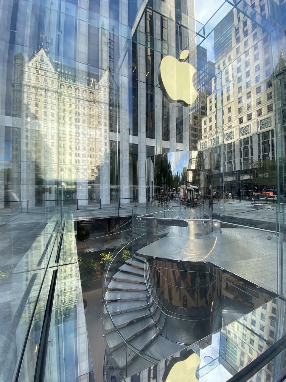 The glass cube reflects the surrounding architecture, such as the iconic Plaza Hotel, located across Fifth Avenue.