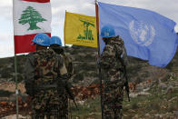 In this Thursday, Dec. 13, 2018 photo, UN peacekeepers hold their flag while standing next to Hezbollah and Lebanese flags, at the site where Israeli excavators are working, near the southern border village of Mays al-Jabal, Lebanon. As Israeli excavators dig into the rocky ground, Lebanese across the frontier gather to watch what Israel calls the Northern Shield operation aimed at destroying attack tunnels built by Hezbollah. But Lebanese soldiers in new camouflaged posts, behind sandbags, or inside abandoned homes underscore the real anxiety that any misstep could lead to a conflagration between the two enemy states that no one seems to want. (AP Photo/Hussein Malla)