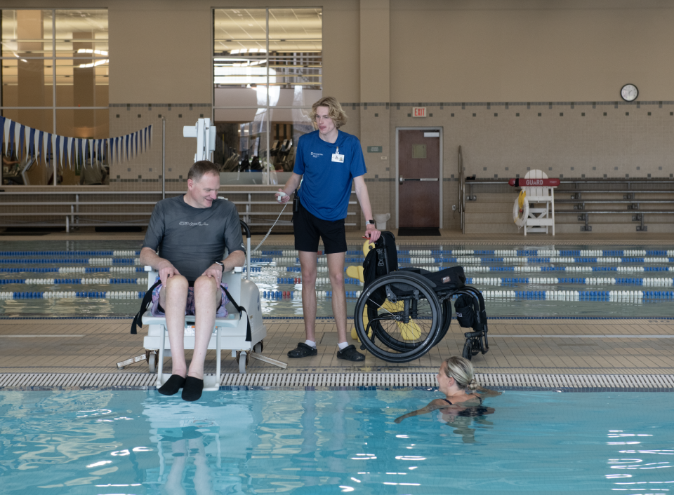 Jason Kolb uses a portable aquatic lift, with the help of his son, Luke Kolb, 18, a lifeguard, to enter the leisure pool at the Cleveland Clinic Akron General Health and Wellness Center in Stow. Amy, his wife, waits in the pool.