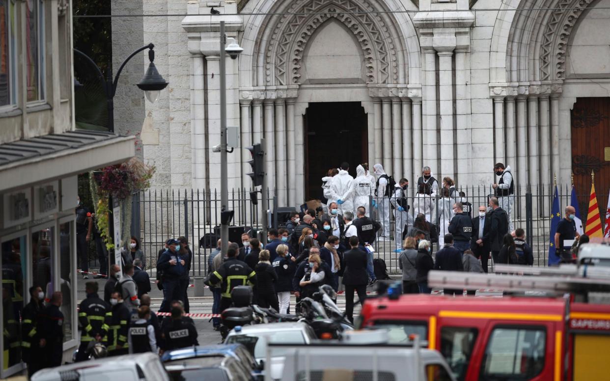 A security camera looms over police officers and forensics specialists at the Notre Dame Church in Nice - Daniel Cole/AP