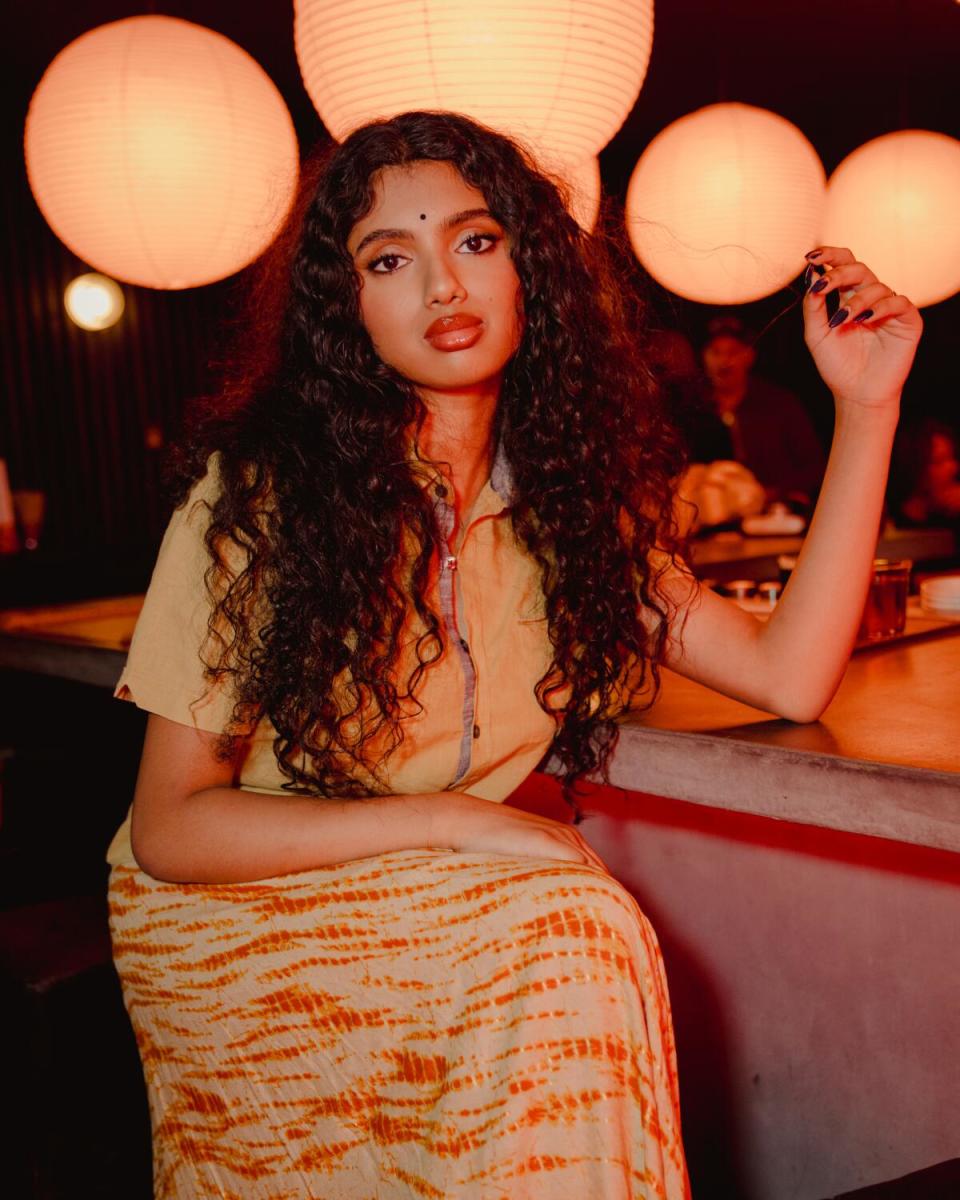 Avantika sits at a bar with globe lights behind her