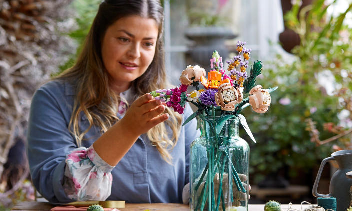 A women inspects a bouquet of LEGO flowers in glass vase.