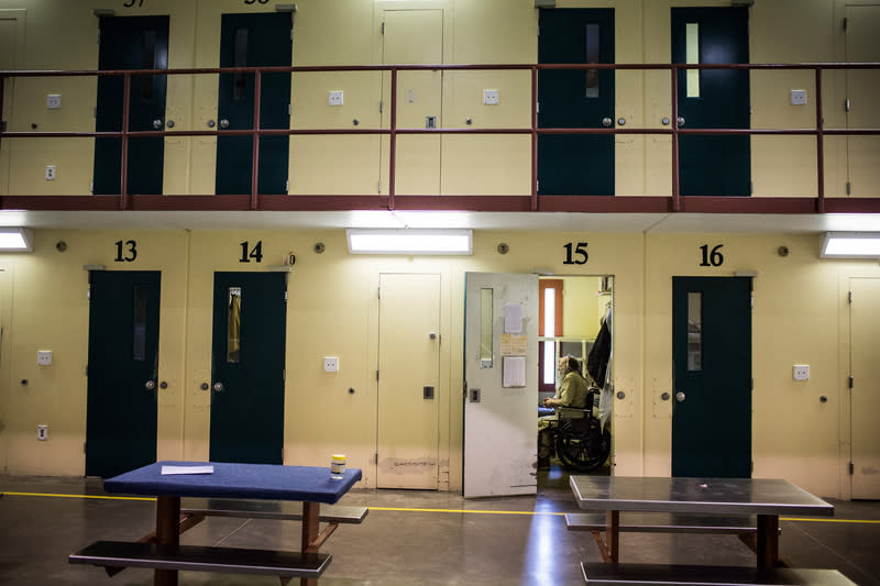 A view from the corridor of a prison with an incarcerated person inside cell doorway.