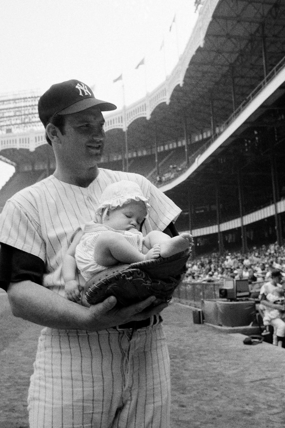 Thurman Munson cradles his daughter Tracy Lynn, age 4 months, in his mitt prior to the game with the Kansas City Royals, Aug. 16, 1970, during Family Day at Yankee Stadium.