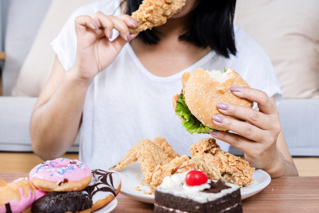 Binge eating disorder concept with woman eating fast food burger, fired chicken , donuts and desserts, over eating obesity