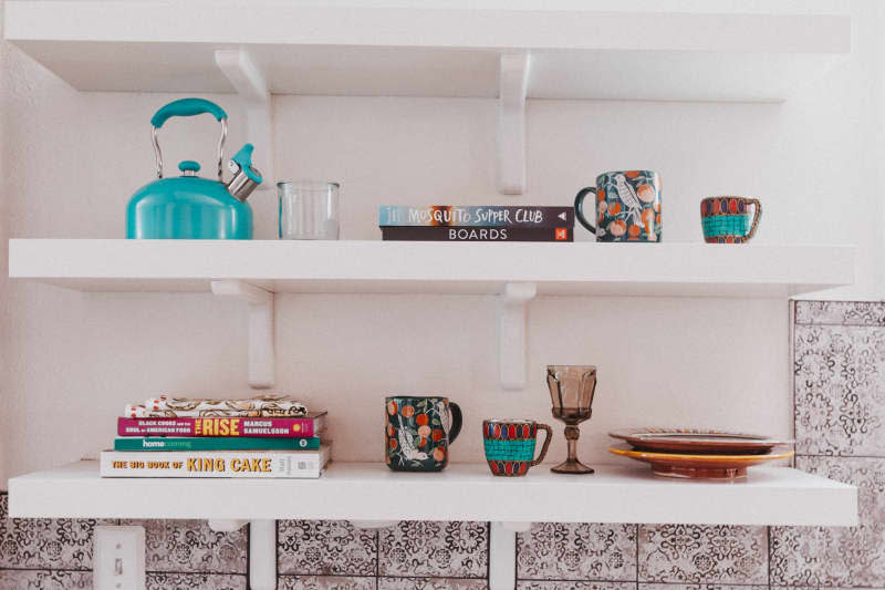 Two white shelves with a kettle, mugs, and books