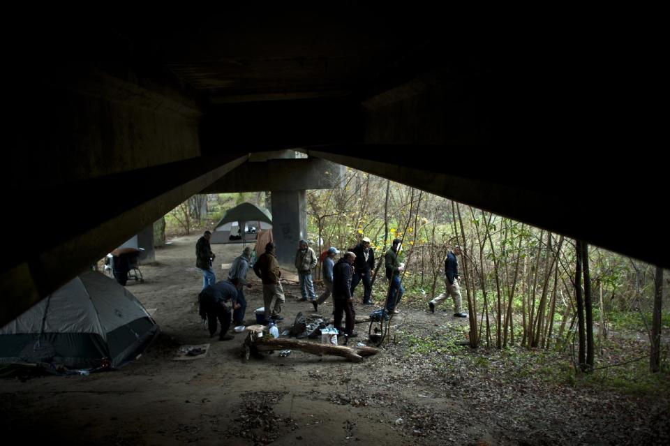 In this Saturday, Dec. 14, 2013 photo, Homeless Liaison Officer Tom Gentner leads a group of homeless men living under a highway overpass in Savannah, Ga. to his patrol car to give them donated items from an Army soldier at Hunter Army Airfield who collected tarps, tents, rope, jackets and other supplies. A large part of Gentner's job is to organize charitable donations and ensure their safety during distribution. (AP Photo/Stephen B. Morton)