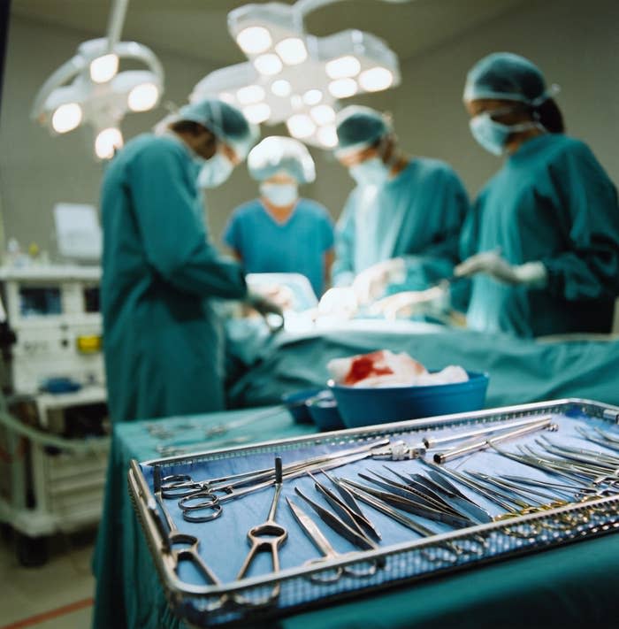 Surgeons perform an operation in an operating room, with a tray of surgical instruments in the foreground