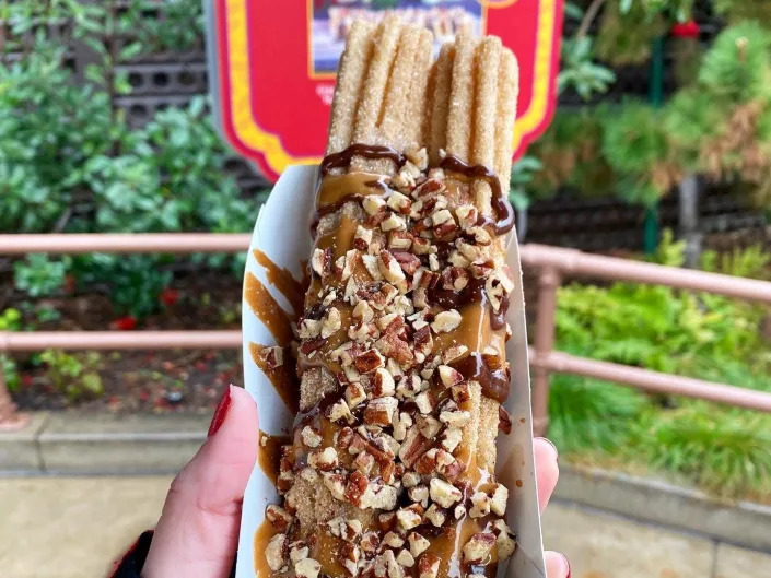 hand holding container of churros covered in chocolate and peanuts