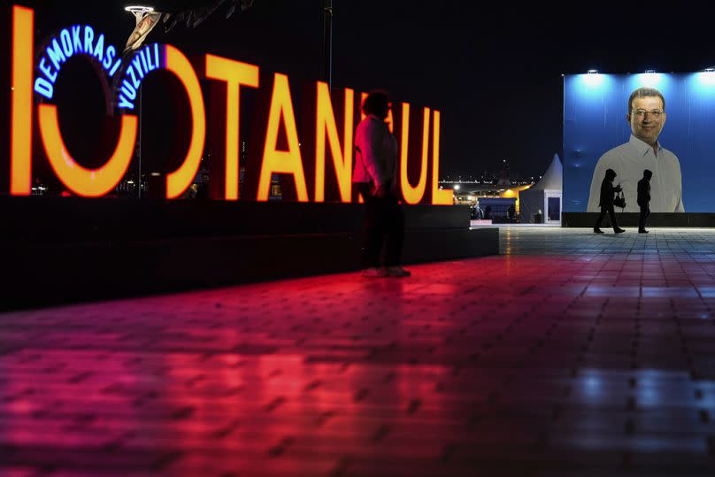 Pedestrians walk past a giant campaign poster of Istanbul Mayor and CHP candidate Ekrem Imamoglu, in Istanbul, March 2024