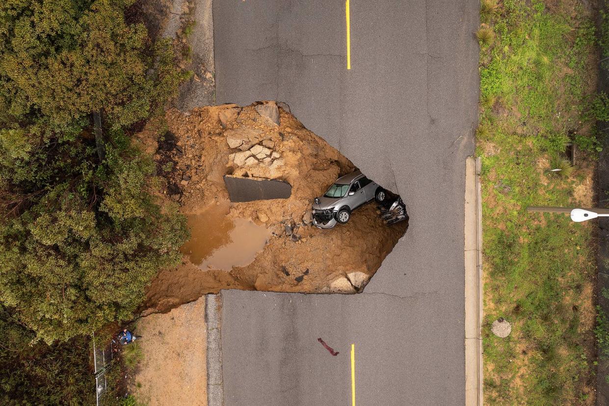 A car and a pickup truck are seen inside a sinkhole as another storm created by a series of atmospheric rivers inundates California on Jan. 10, 2023, in Los Angeles.