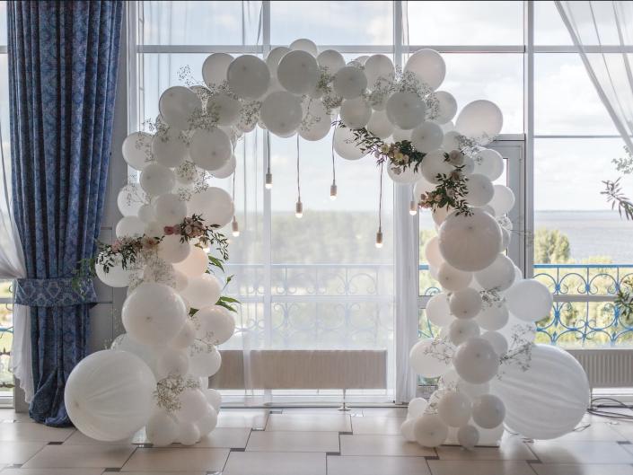 arch of white balloons inside an event space with large, open windows
