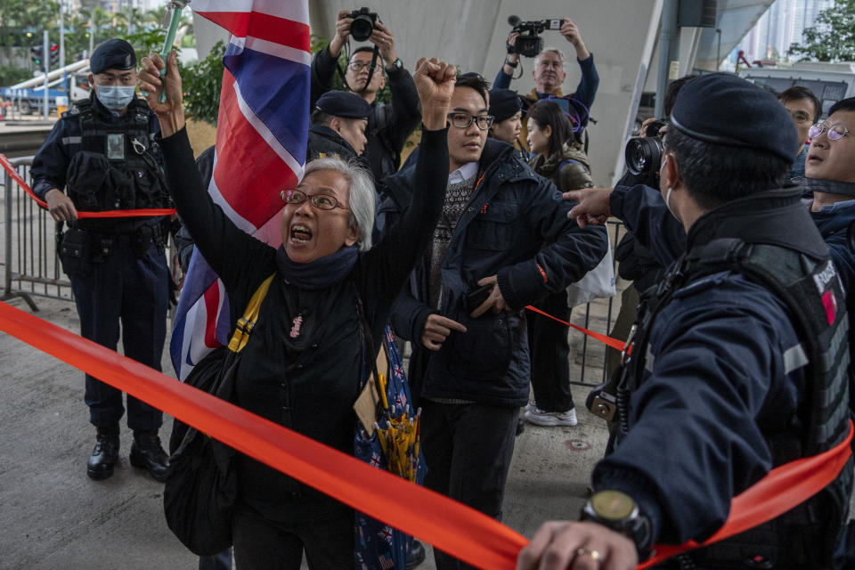 Activist Alexandra Wong holding a British flag shouts behind a police line set up outside West Kowloon Magistrates' Courts, where activist publisher Jimmy Lai's trial is scheduled to open, in Hong Kong, Monday, Dec. 18, 2023. A landmark national security trial opened Monday in Hong Kong for prominent activist publisher Jimmy Lai, who faces a possible life sentence if convicted under a law imposed by Beijing to crush dissidents. (AP Photo/Vernon Yuen)